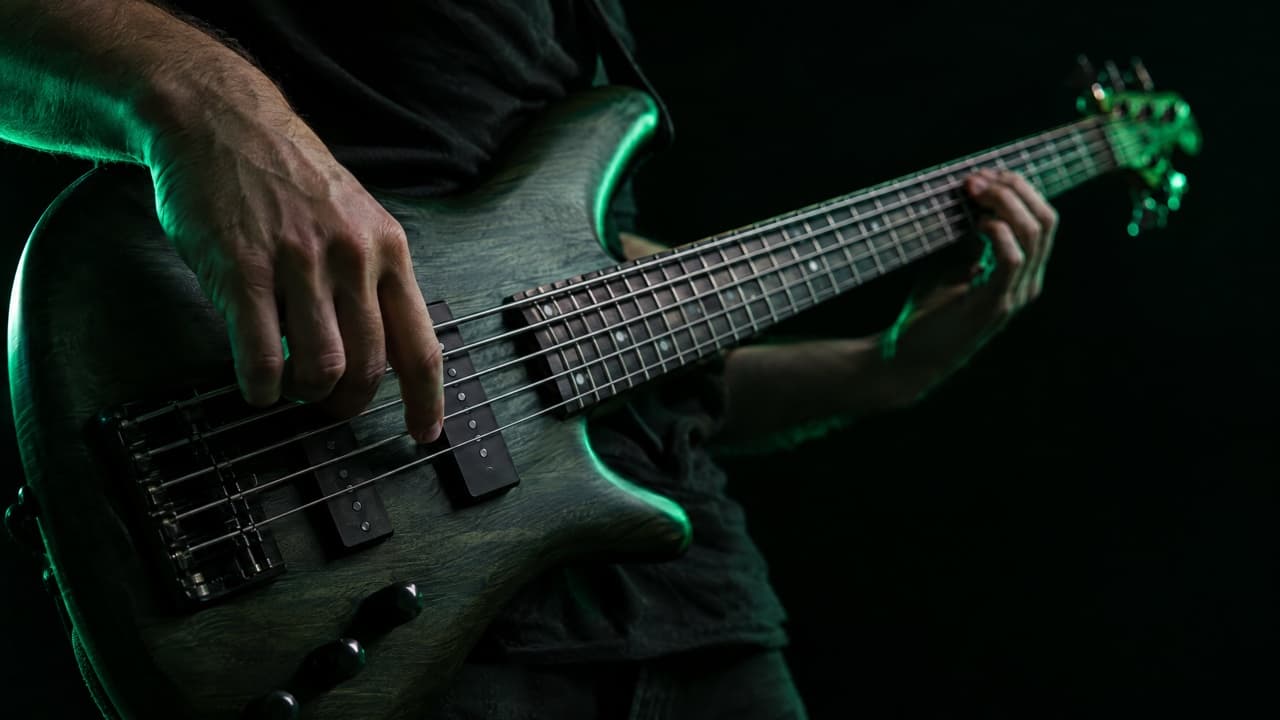 Finger zupfen die tiefe Saite eines Fünfsaiter-Basses in einem dunklen Studio